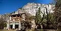 Photograph of The Ahwahnee in winter snow, amidst bare trees with the dramatic walls of Yosemite Valley rising behind.