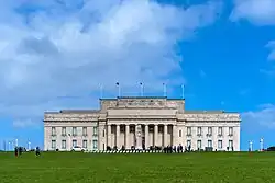 Large neoclassical-style building with a forecourt featuring a Cenotaph on a Court of Honour. Above the front porch of the building is inscribed a funeral oration attributed to the Greek General Pericles, which reads "MCMXIV – MCMXVIII / The whole earth is the sepulchre of famous men / They are commemorated not only by columns and inscriptions in their own country / but in foreign lands also; by memorials graven not on stone / but on the hearts of men." A New Zealand flag atop the building is flown at half-mast. Banners hanging between the columns advertise exhibitions about volcanoes, and Charles Darwin.