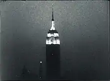Grainy, black-and-white still frame of the illuminated Empire State Building against the night sky