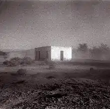 A grainy black-and-white photo of a building in the middle of a desert.