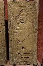 An Eastern Han carved stone tomb door showing a man wearing trousers underneath a long robe with a jinze hat, stored in Sichuan Provincial Museum in Chengdu