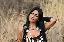 Kelly Derrickson in traditional costume standing in the tall grasslands on Okanagan territory