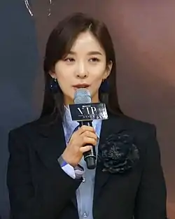 Lee wearing black suit and holding a mic in October 2019