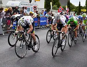 A number of cyclists are pictured sprinting along a road with a crowd watching them