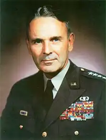 Middle-aged man with graying dark hair parted slightly off center. He wears a green dress uniform, with suit and tie, is clean-shaven, and has four stars on his shoulder to indicate his rank.