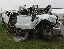 The severely damaged front left corner of a white stretch limousine