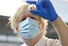 Johnson, wearing a facemask and surgical glove, examines a vial of vaccine