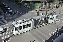 An overhead view of a white streetcar crossing an intersection, passing under traffic signals.