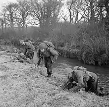 Soldiers from the division training, take cover along a river bank.